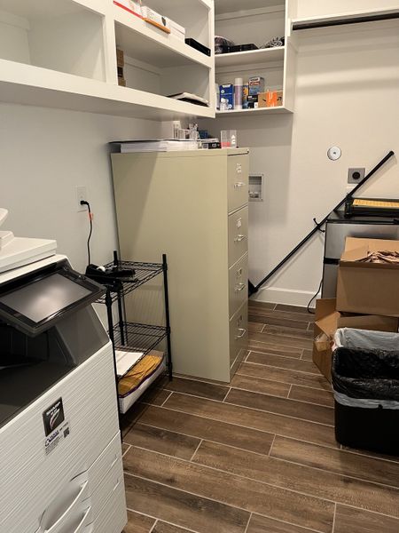 A functional utility room with organized shelving, a filing cabinet, and a modern printer on sleek wood-look tiles.