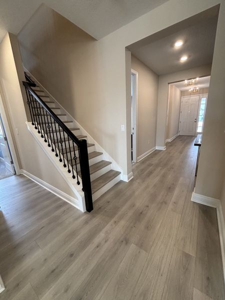 A warm and inviting hallway with wood-look flooring, elegant lighting fixtures, and soft beige walls, creating a welcoming entrance in Crossroads at Kelly Park by Dream Finders Homes (Apopka, FL).