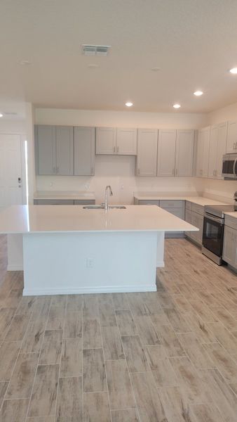 A modern kitchen with sleek gray cabinets, a central island, and wood-look tile flooring.