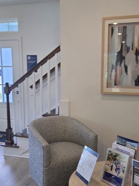 A cozy corner with modern artwork, a plush gray chair, and elegant staircase, creating a welcoming entrance.