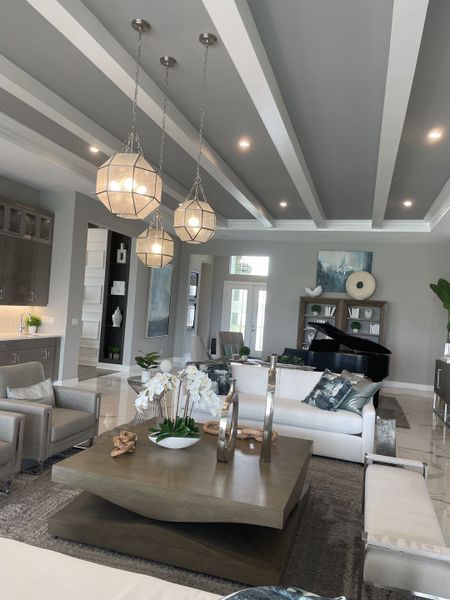 Elegant living room with modern lighting, coffered ceiling, plush seating, and a grand piano centerpiece.