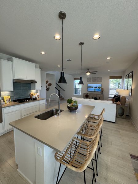 A modern kitchen with pendant lighting, sleek countertops, wicker bar stools, and an open layout.