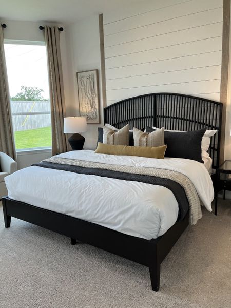 A cozy bedroom featuring a stylish black bedframe, elegant pillows, and a shiplap accent wall with warm natural light.