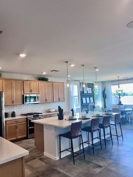 Spacious kitchen with light wood cabinets, a large island, modern lighting, and a dining area with ample natural light. Spacious kitchen with light wood cabinets, a large island, modern lighting, and a dining area with ample natural light.