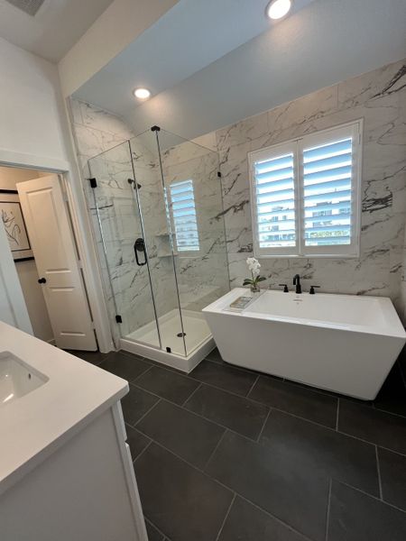 A modern bathroom featuring a marble-tiled shower, sleek bathtub, and stylish lighting with dark floor tiles.