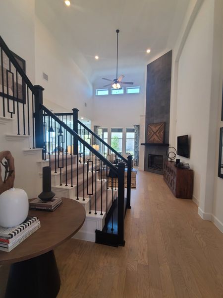 A spacious living area with a high ceiling, elegant staircase, and cozy fireplace. Steps lead up to the well-lit upper floor.