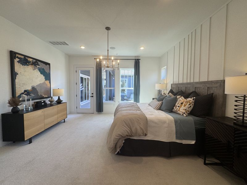 A spacious bedroom with a cozy bed, modern chandelier, and elegant decor featuring neutral tones and large artwork.