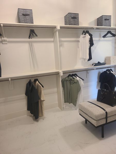 A spacious walk-in closet with modern shelving, white tiled floors, and cozy bench seating. A spacious walk-in closet with modern shelving, white tiled floors, and cozy bench seating.