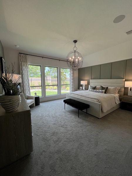 A spacious bedroom with a modern chandelier, large windows, neutral tones, and elegant furnishings.