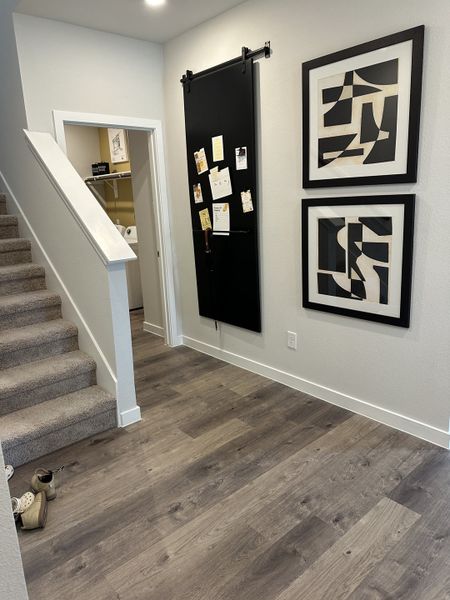 A modern hallway with sleek wood flooring, abstract art, plush carpeted stairs, and a black sliding barn door.