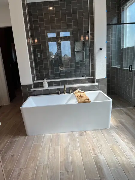 A modern bathroom featuring a white bathtub, gray tiled walls, and sleek wood-patterned flooring.