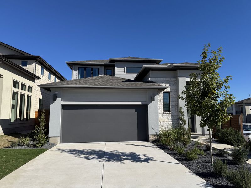 A contemporary two-story home with a dark gray garage and minimalist landscaping in Old Town East by Perry Homes (Pflugerville, TX).