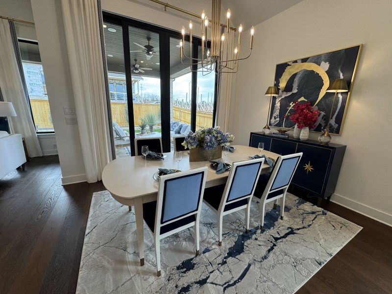 A chic dining area with a sleek table, elegant chandelier, and large abstract art, opening up to a stylish patio space.