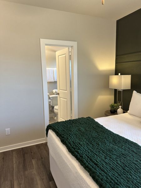 Modern bedroom with dark accent wall, cozy bedding, and en-suite bathroom featuring elegant decor and warm lighting.