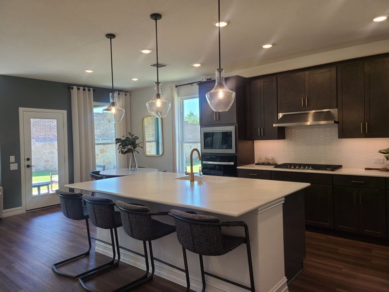 A modern kitchen featuring a sleek island, pendant lights, dark cabinetry, and stainless steel appliances. A modern kitchen featuring a sleek island, pendant lights, dark cabinetry, and stainless steel appliances.