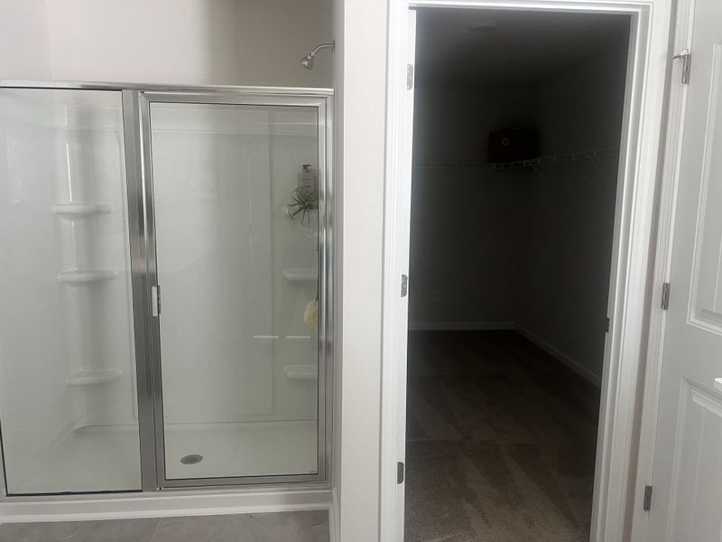 A modern bathroom featuring a clear glass shower and an adjacent walk-in closet, offering ample storage space.
