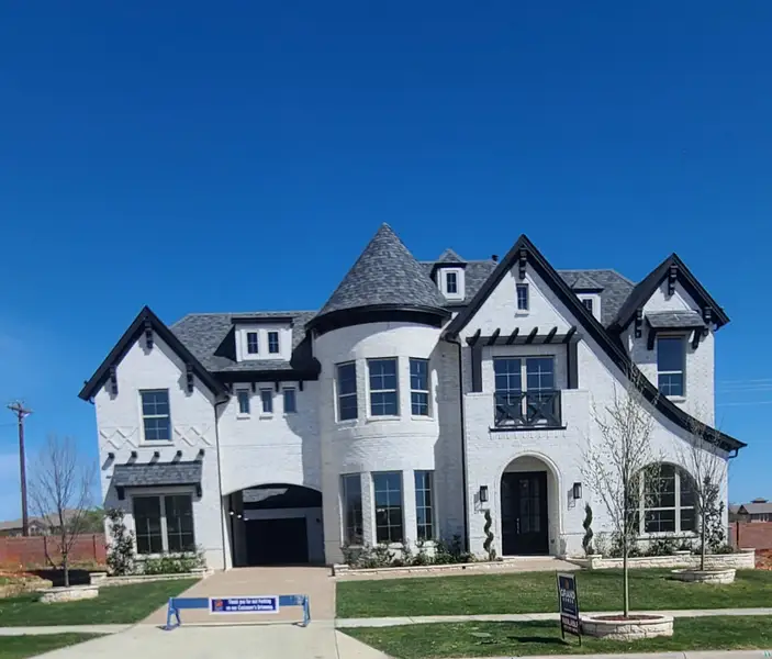 A grand white brick home with turrets and lush landscaping in Silverleaf Estates by Grand Homes (Frisco, TX).