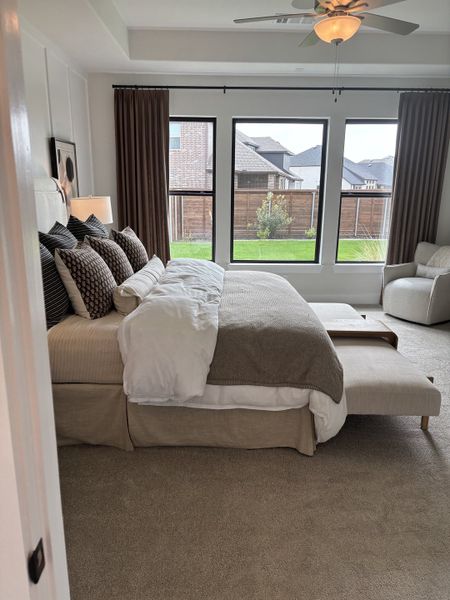 A cozy bedroom with plush bedding, large windows, elegant curtains, and relaxing neutral tones.