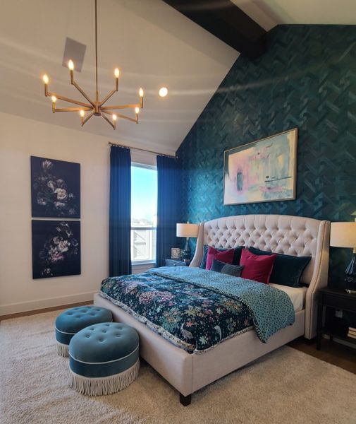 A chic bedroom featuring a tufted headboard, patterned bedding, teal accent wall, and modern chandelier.