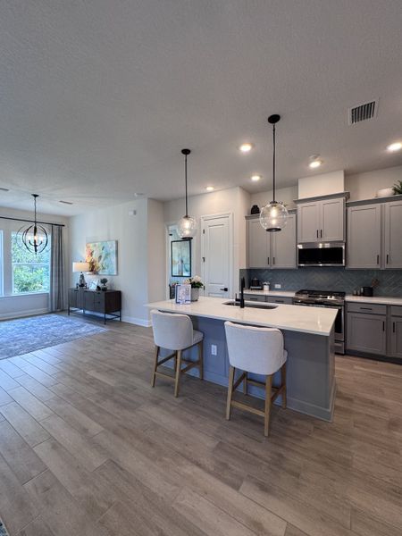 Open-concept kitchen with sleek grey cabinetry, pendant lighting, and wood-look flooring for a modern, cozy vibe. Open-concept kitchen with sleek grey cabinetry, pendant lighting, and wood-look flooring for a modern, cozy vibe.