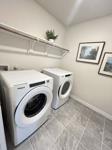 A modern laundry room with sleek appliances, tiled flooring, wall shelves, and framed artwork. A modern laundry room with sleek appliances, tiled flooring, wall shelves, and framed artwork.