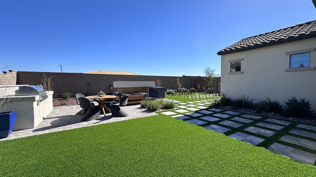 A well-manicured backyard with a modern patio, outdoor seating, and chess set on artificial turf.