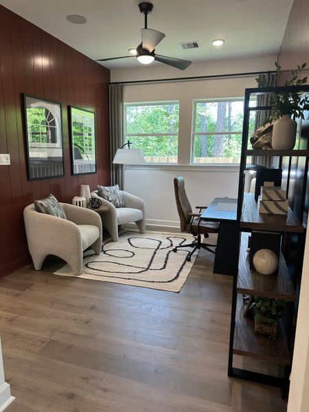 A cozy office space with plush chairs, large windows, modern decor, and a stylish ceiling fan.