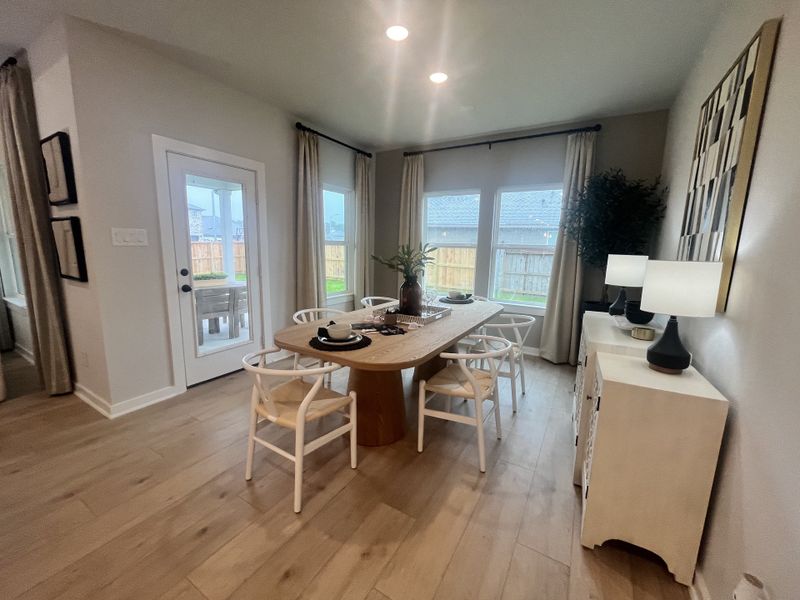 A cozy dining space with a wooden table, elegant chairs, and soft lighting from modern lamps, opens to a backyard view.