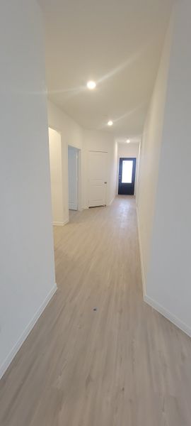 A bright hallway with wood flooring, white walls, and modern lighting fixtures creating an inviting entrance space.
