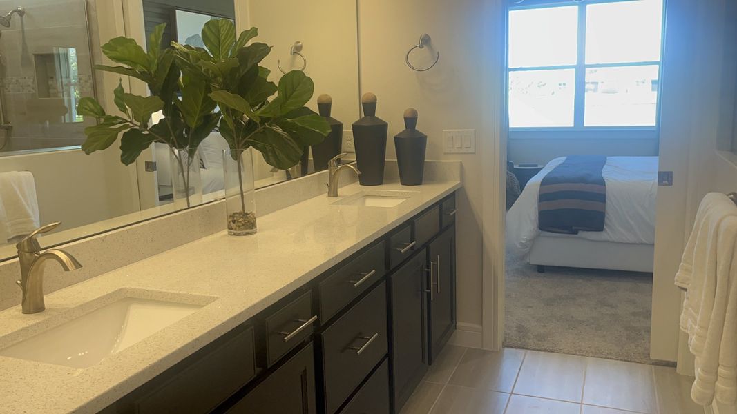 A sleek bathroom featuring a quartz double vanity, chic black cabinets, and tasteful decor with lush greenery.