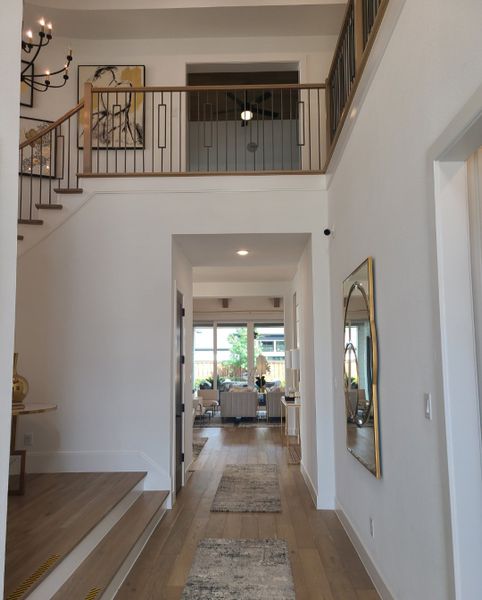 An elegant foyer with warm wood floors, modern art, and railing, leading to an airy living room with large windows. An elegant foyer with warm wood floors, modern art, and railing, leading to an airy living room with large windows.