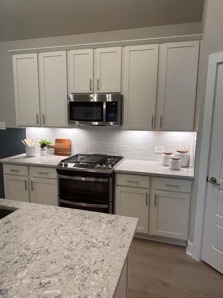 A modern kitchen with sleek granite countertops, white cabinetry, a stainless steel microwave, and stylish lighting.