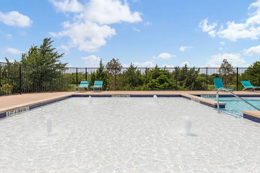 Outdoor community pool with water jets, lounge chairs, and black iron fence surrounding the deck area