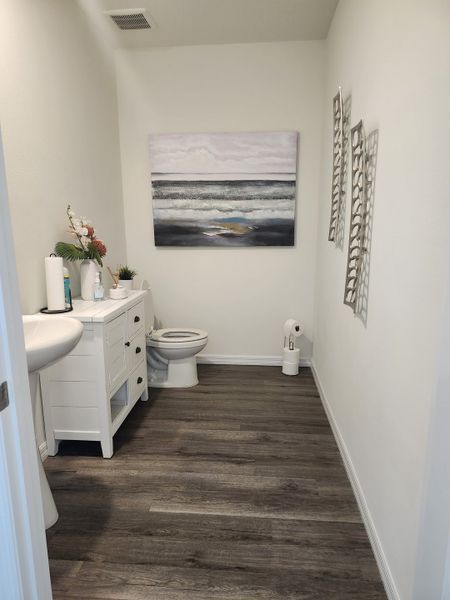 A modern bathroom with dark wood floors, white vanity, and ocean-themed artwork for a calming atmosphere.