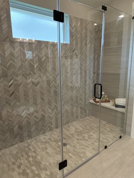 A luxurious shower with herringbone and hexagon tiles, featuring a modern glass door and built-in shelf.