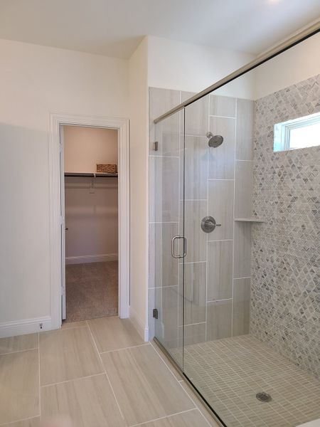 A spacious bathroom with a glass shower featuring modern tilework and an adjacent walk-in closet for added convenience.