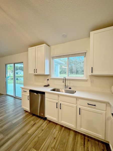 A bright kitchen with stainless steel appliances, white cabinetry, and a large window offering a scenic view.