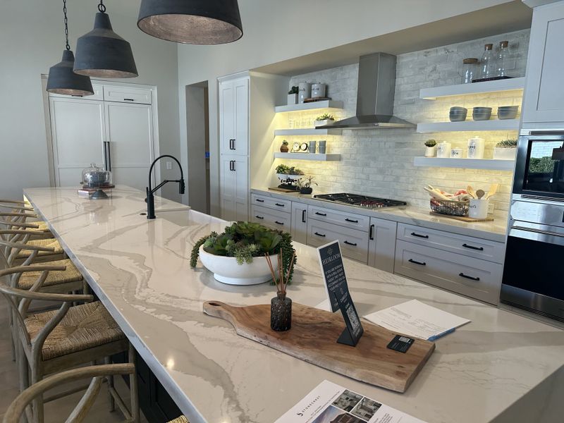 A modern kitchen with an expansive marble island, pendant lighting, and sleek cabinetry featuring open shelves.
