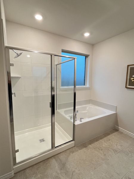 A modern bathroom with a glass shower, a cozy bathtub, and recessed lighting on neutral tiled floors.