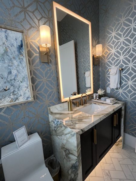 A luxurious bathroom with geometric wallpaper, marble vanity, brass fixtures, and elegant lighting.