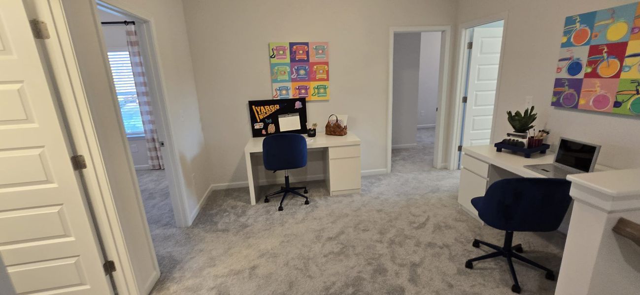 A cozy study area with dual desks, vibrant artwork, and plush carpeting.