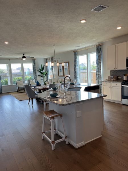 An open-concept kitchen and dining area with a large island, elegant lighting, and expansive windows flooding light in.