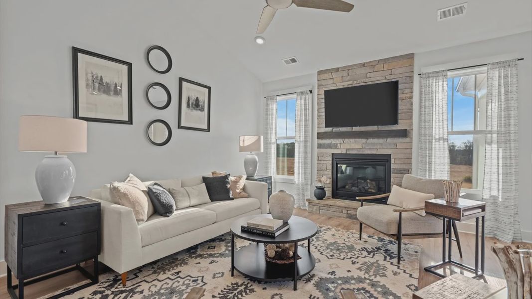 Two story ceiling family room with cozy stone fireplace, large windows, and ceiling fan at Pelham Crossing by DRB Homes