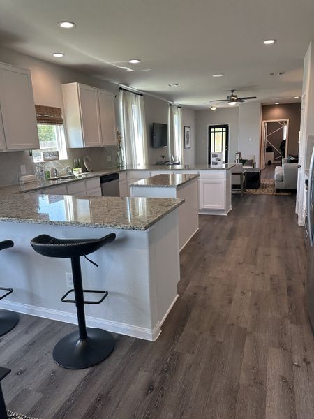 A modern kitchen features granite countertops, dark wood floors, and sleek white cabinetry with barstool seating.