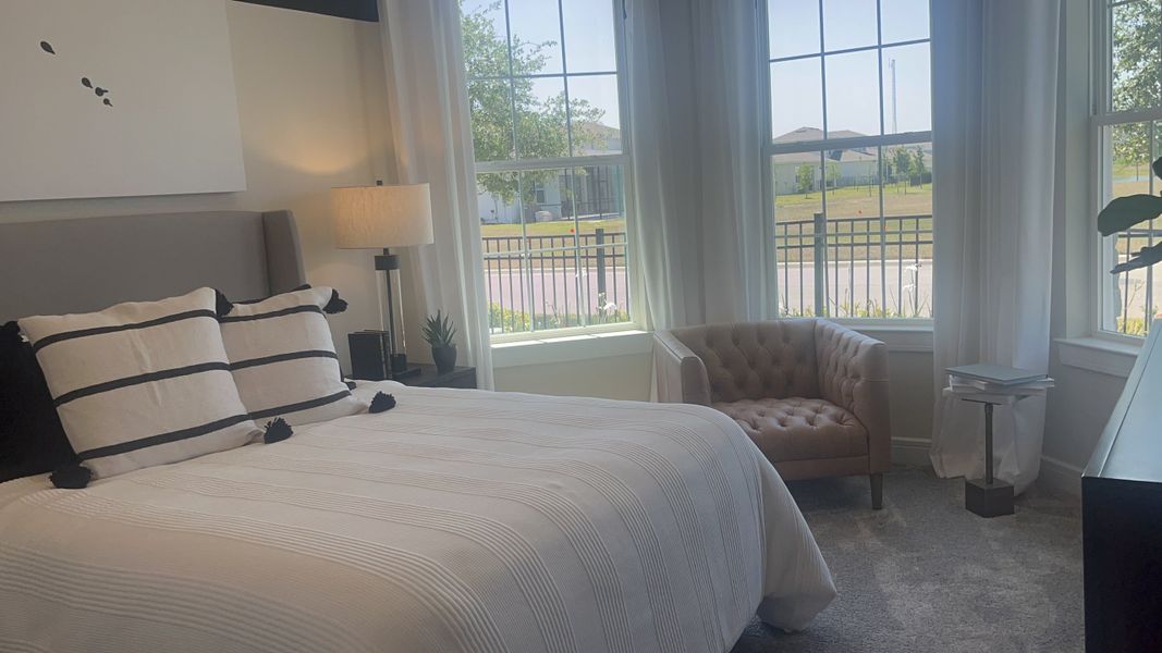 A cozy bedroom featuring a plush bed with striped pillows, a tufted chair, and large windows that brighten the space.
