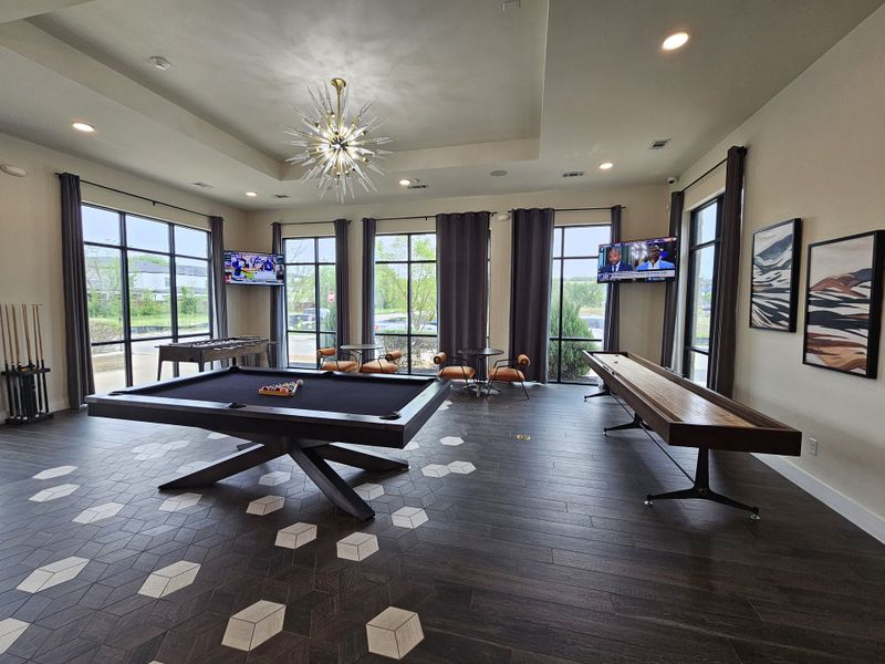 A chic game room with a modern pool table, shuffleboard, elegant lighting, and large windows for natural light.
