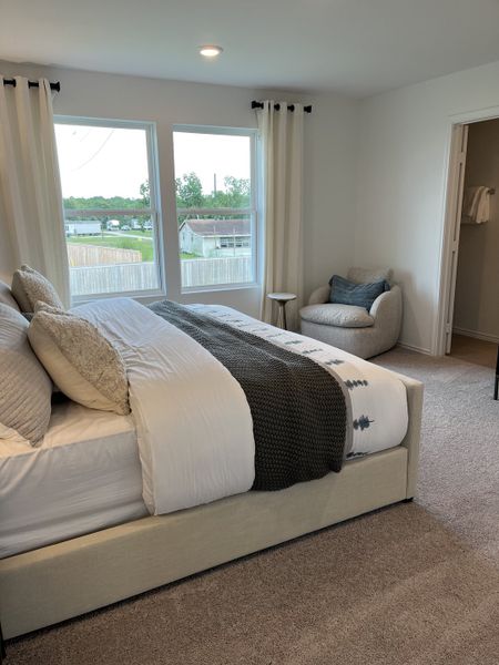 A cozy bedroom featuring a plush bed, neutral decor, large windows with views, and a comfy reading chair.