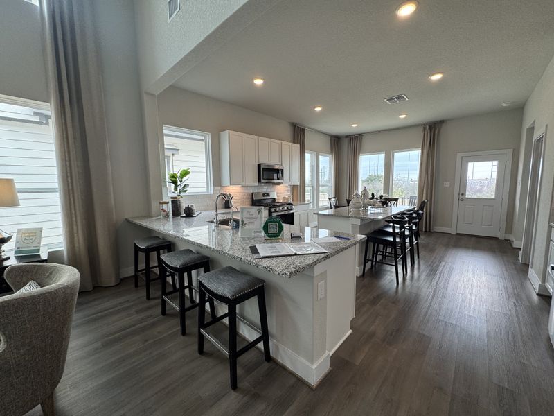 An open kitchen with a granite island, wood floor, white cabinets, and ample lighting creates a warm, modern space. An open kitchen with a granite island, wood floor, white cabinets, and ample lighting creates a warm, modern space.