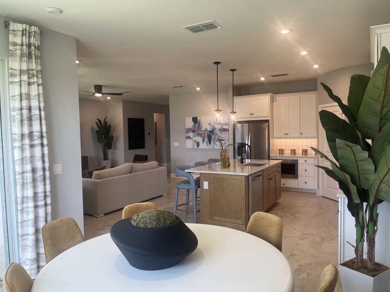 A modern open-concept kitchen and living area with stylish decor, featuring sleek furniture, pendant lighting, and indoor plants.