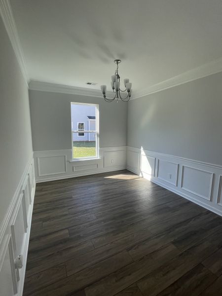 A bright room featuring elegant wainscoting, a modern chandelier, and sleek wood flooring.
